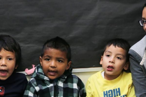 Image of a Cal State LA female student sitting next to three small children who appear to be singing. 