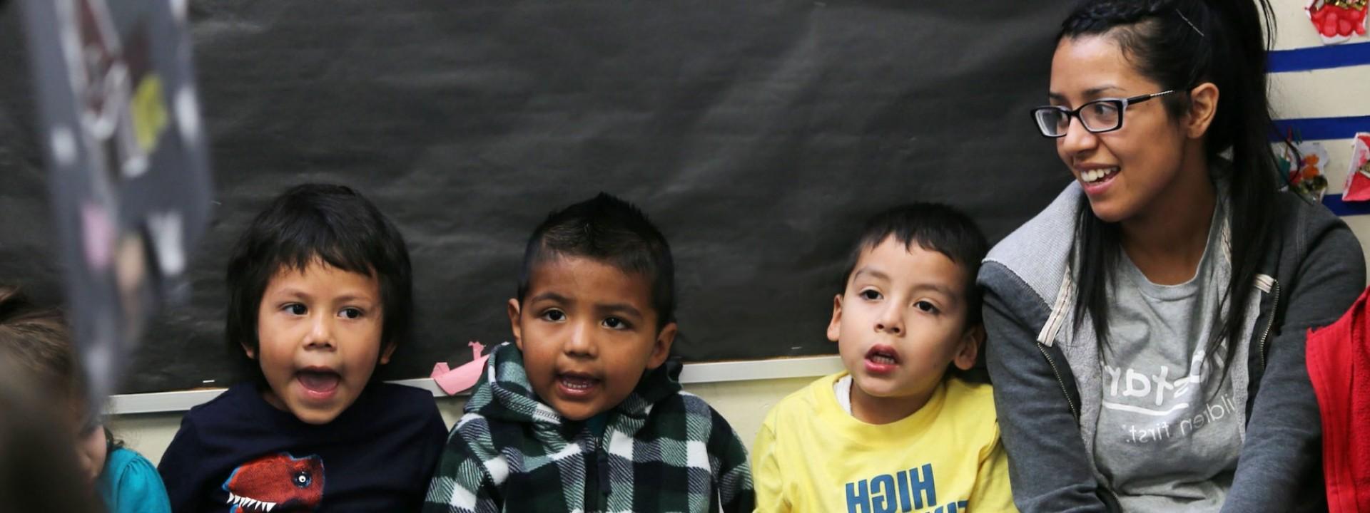 Image of a Cal State LA female student sitting next to three small children who appear to be singing. 